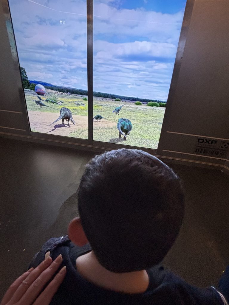 Kind beobachtet Dinosaurier durch Fenster in der DinoXperience Königswinter