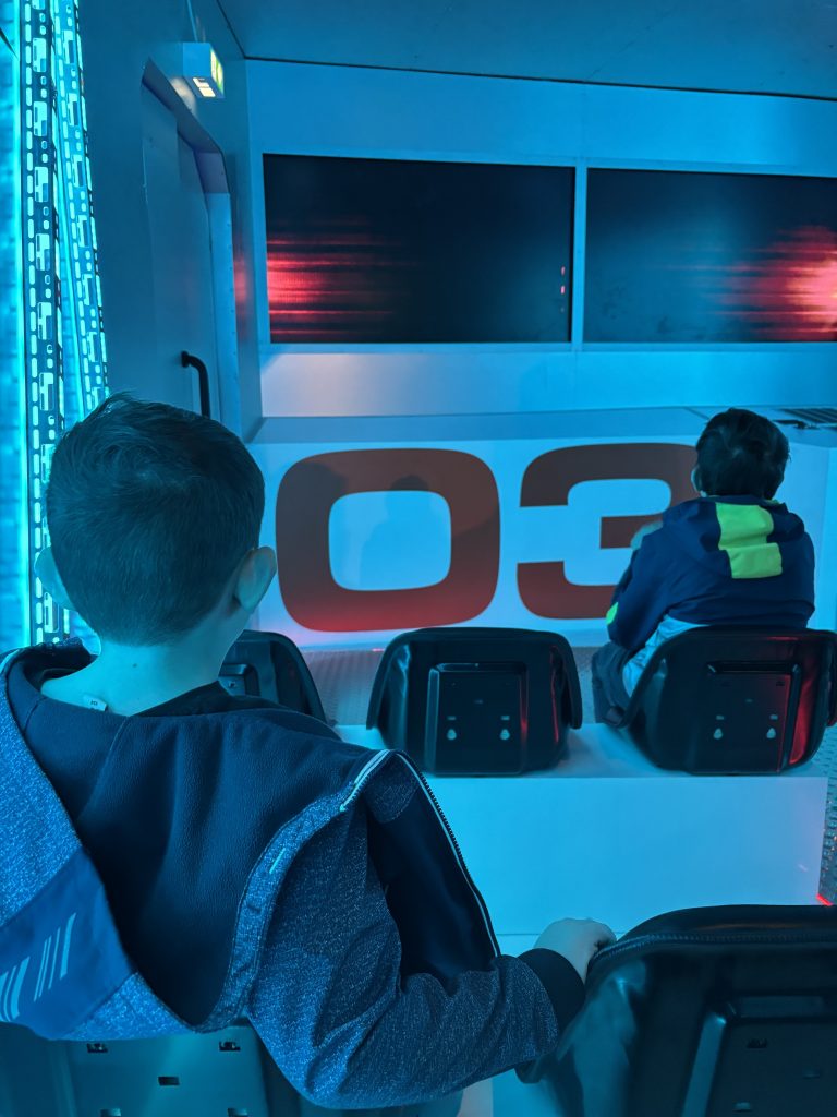 Fabi und Flo sitzen im Fahrzeug während der DinoXperience Fahrt durch die Dinosaurier Welt