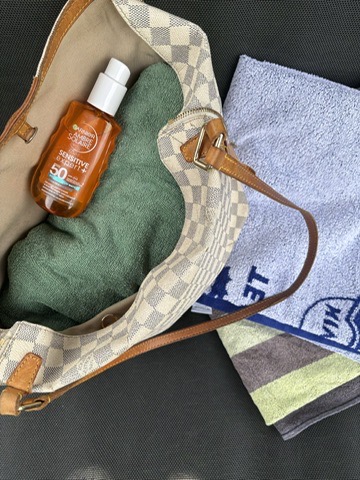 Garnier Sonnenschutz Spray in einer Tasche mit Handtuch
