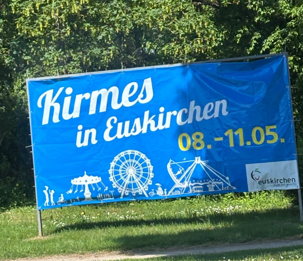 Großes blaues Werbeschild der Donatus Maikirmes Euskirchen 2026 am Straßenrand mit Datum der Kirmesveranstaltung.